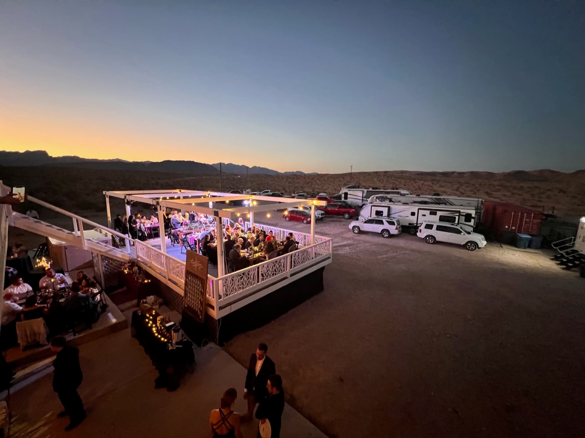Twilight aerial view of the fully lit two-level deck packed with guests, desert stretching beyond