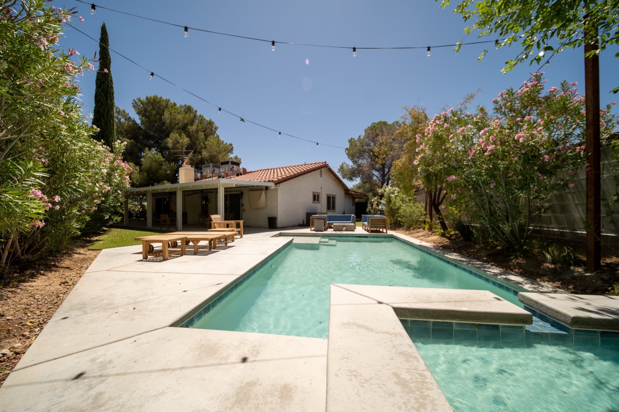Wide daytime view of the backyard pool, spa, and covered patio with the house in the background