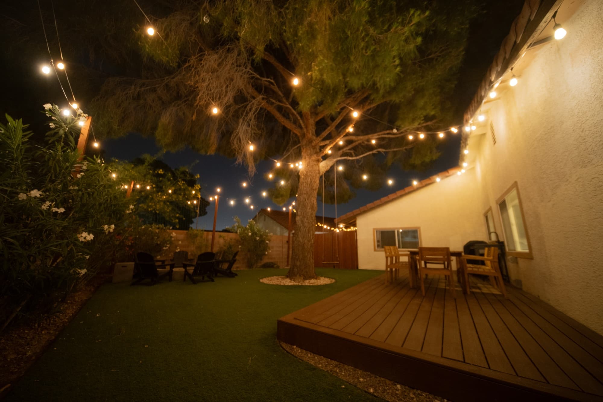 Wood deck dining area strung with string lights around a mature tree at night