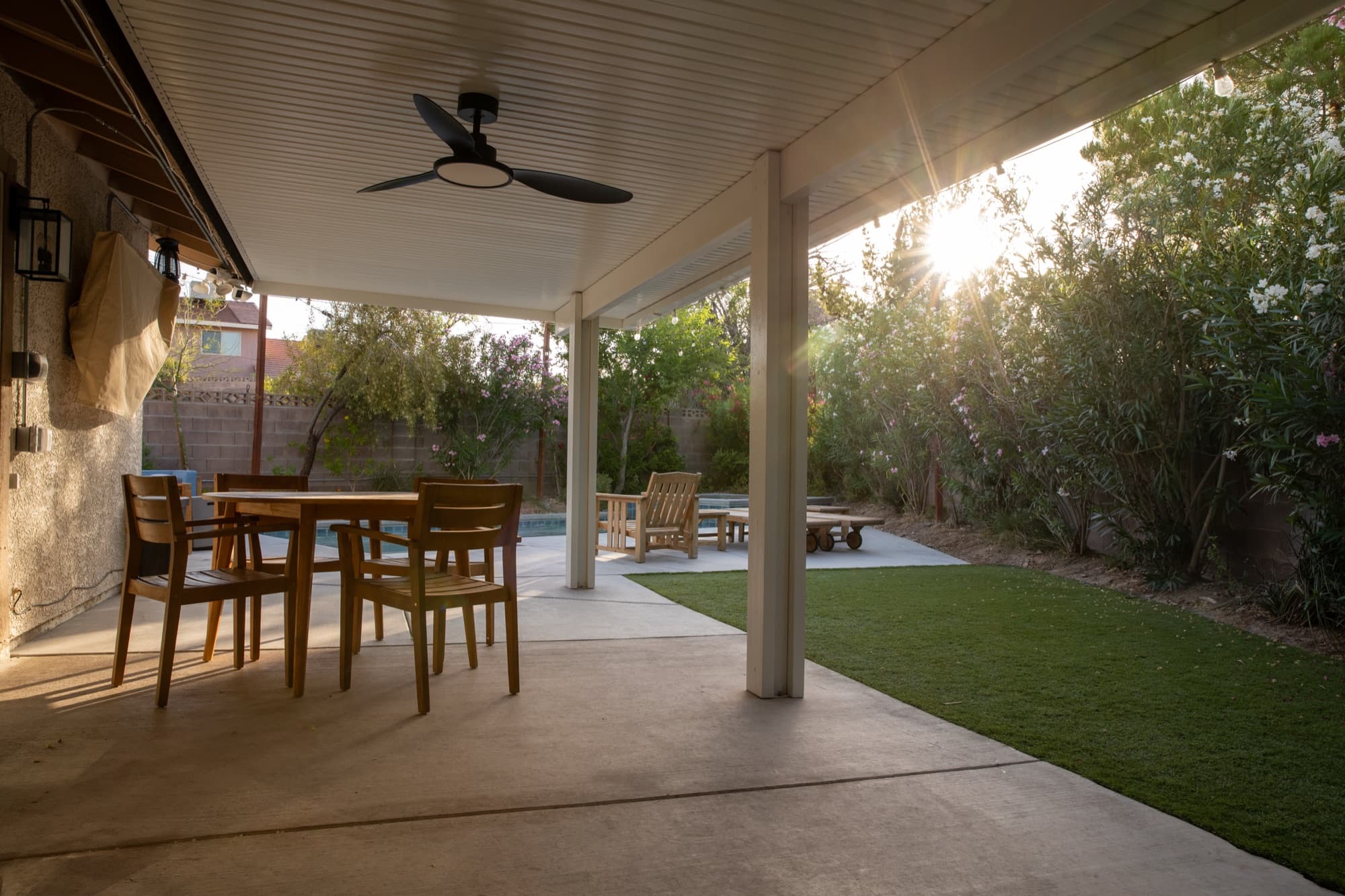 Covered patio dining table with ceiling fan overlooking the pool and turf lawn