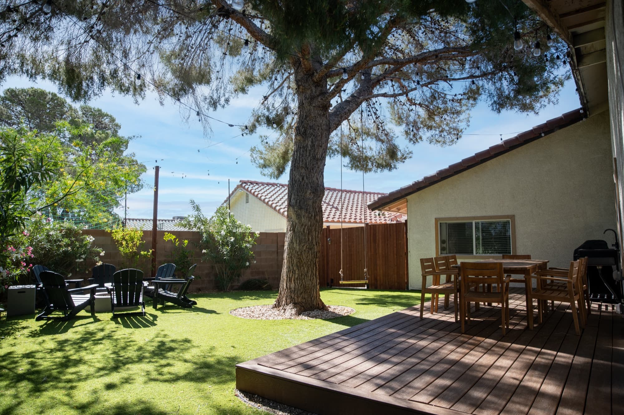 Daytime view of the full backyard with shade tree, wood deck, and fire pit seating area